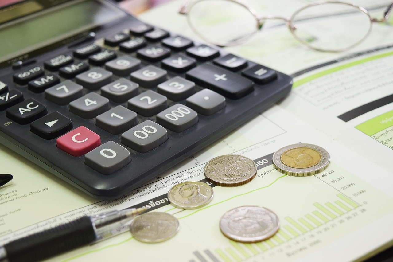 آلة حاسبة على مكتب بجانب عملات معدنية وأوراق عليها رسوم بيانية
