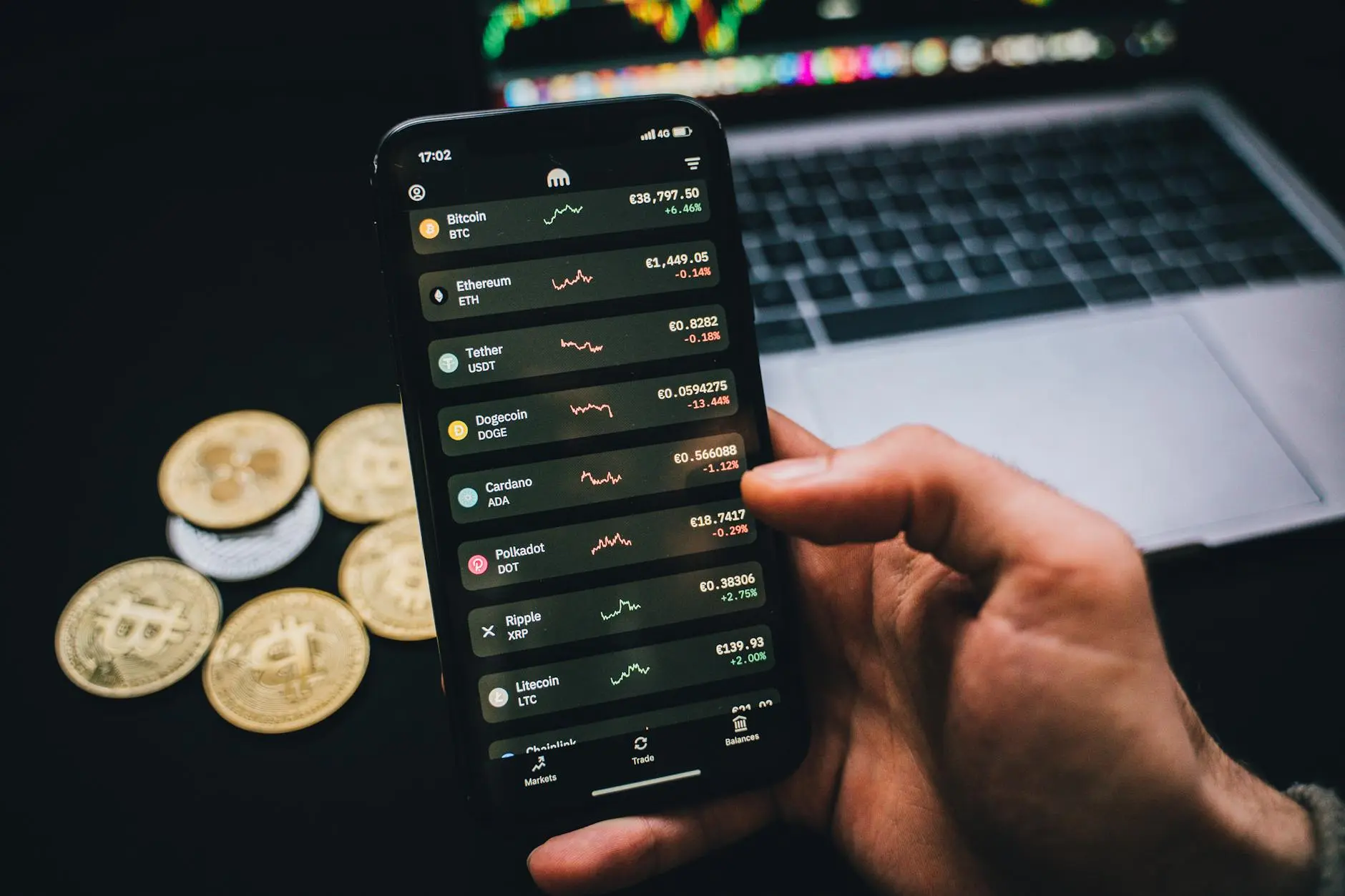 A smartphone displaying cryptocurrency prices next to physical coins on a desk.