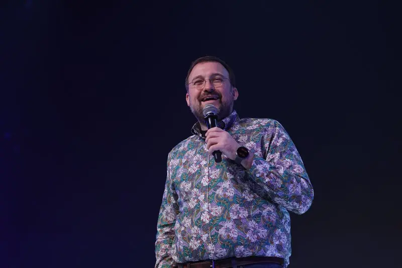 Charles Hoskinson speaking into a microphone while wearing a floral print shirt