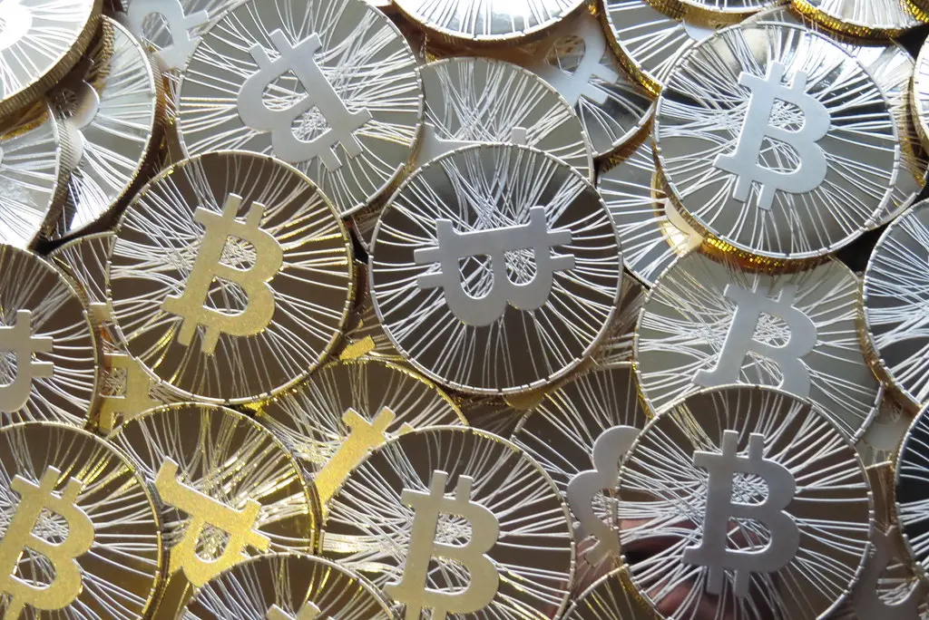 A close-up pile of gold-colored physical Bitcoin coins featuring the Bitcoin symbol.