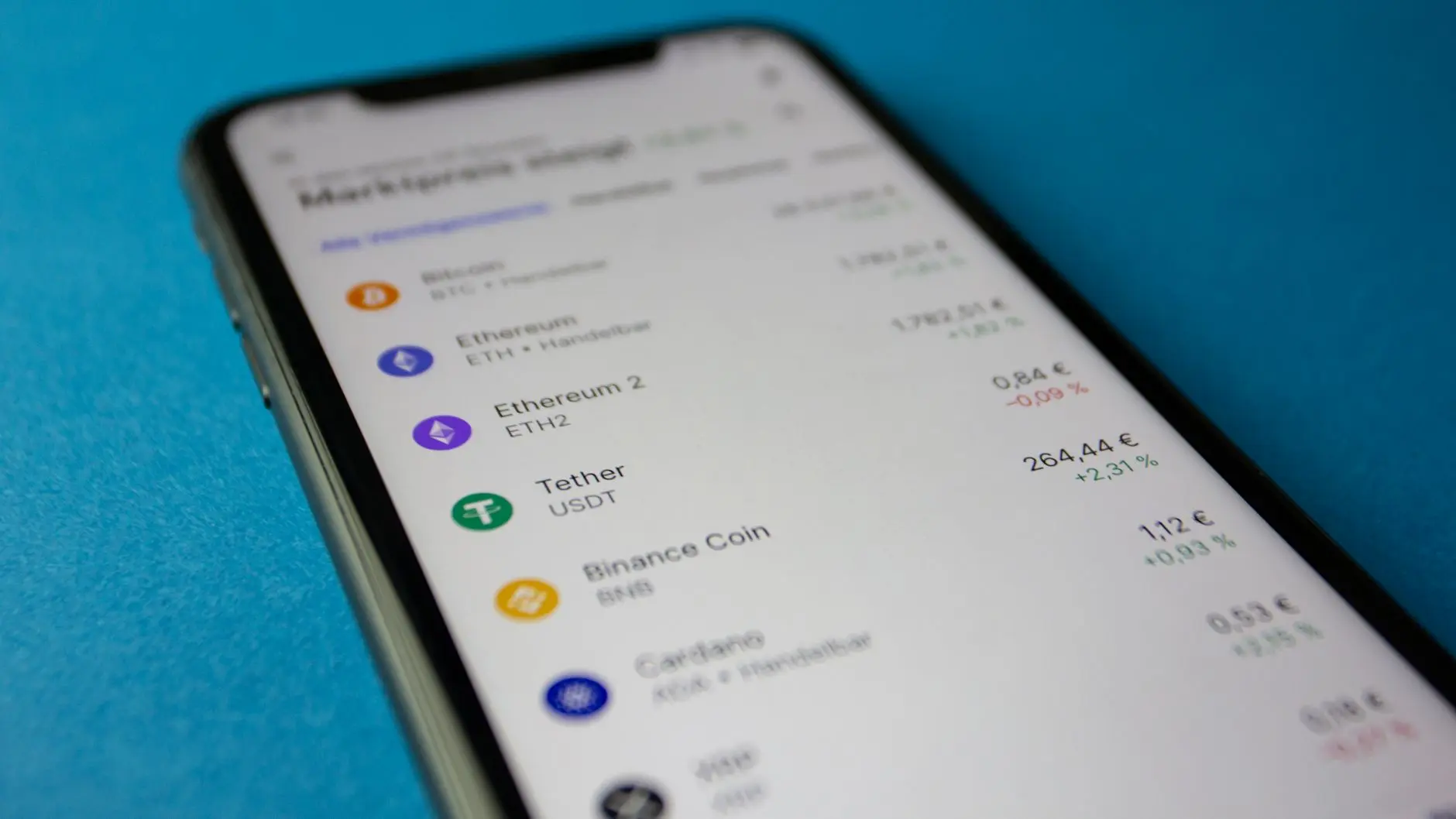 A smartphone screen displaying a list of cryptocurrencies including Bitcoin, Ethereum, and Cardano ADA