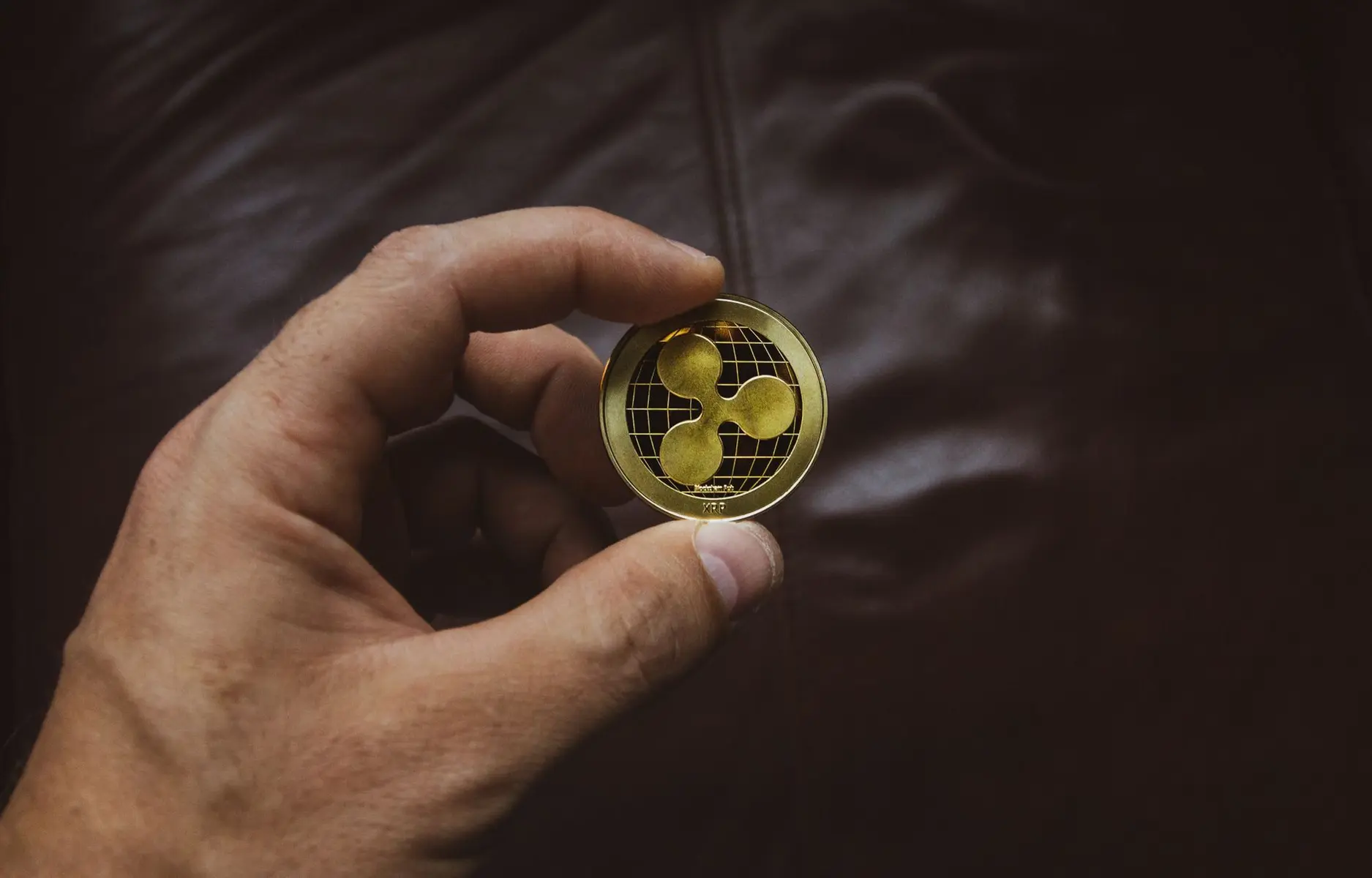 A person's hand holding a gold-colored physical Ripple XRP commemorative coin