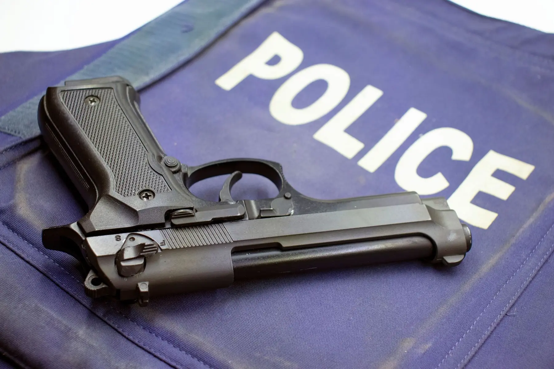 A black semi-automatic handgun resting on a blue police vest with the word POLICE in white letters