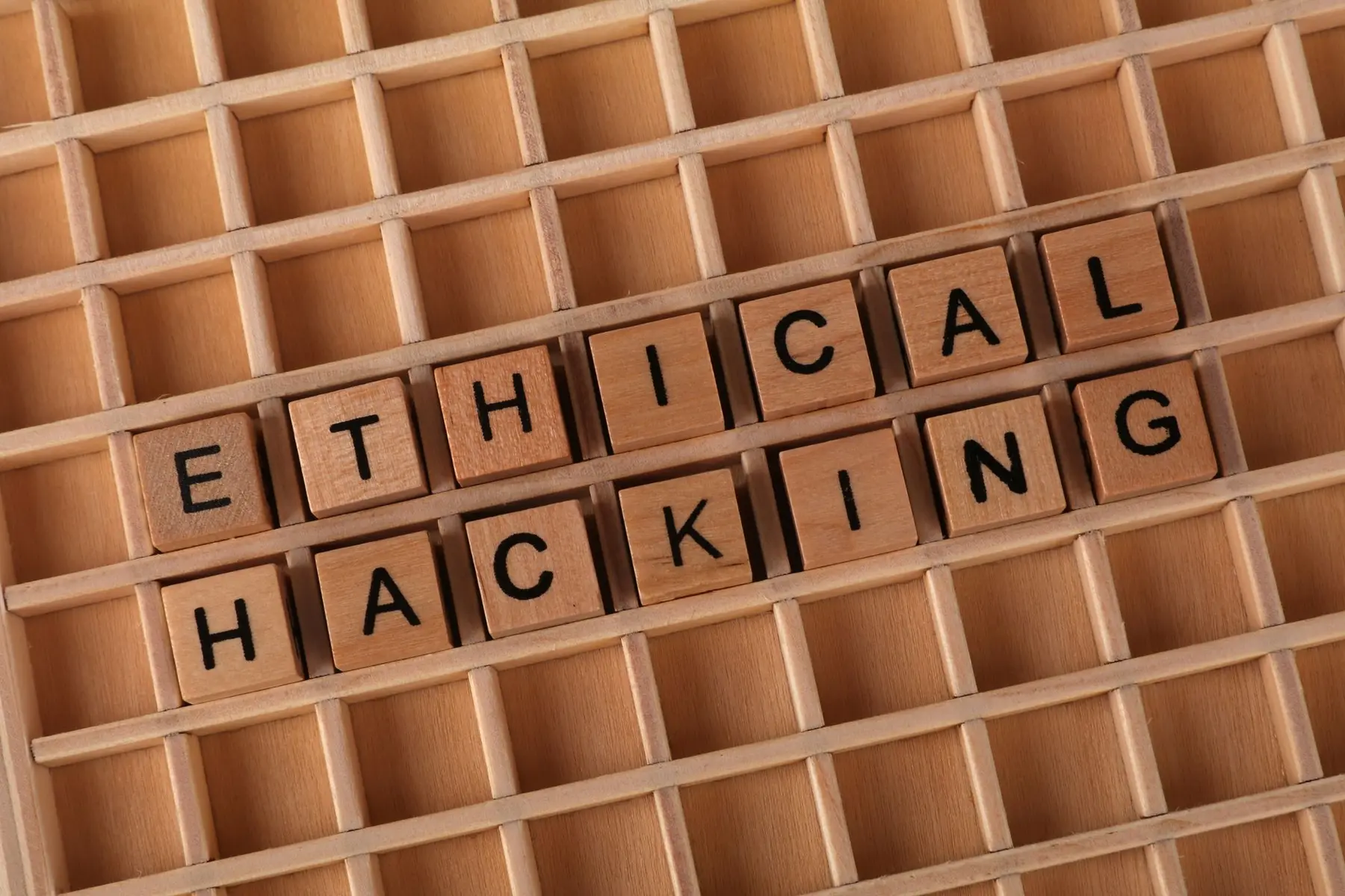 Wooden letter blocks spelling 'ETHICAL HACKING' arranged in a grid-like wooden tray