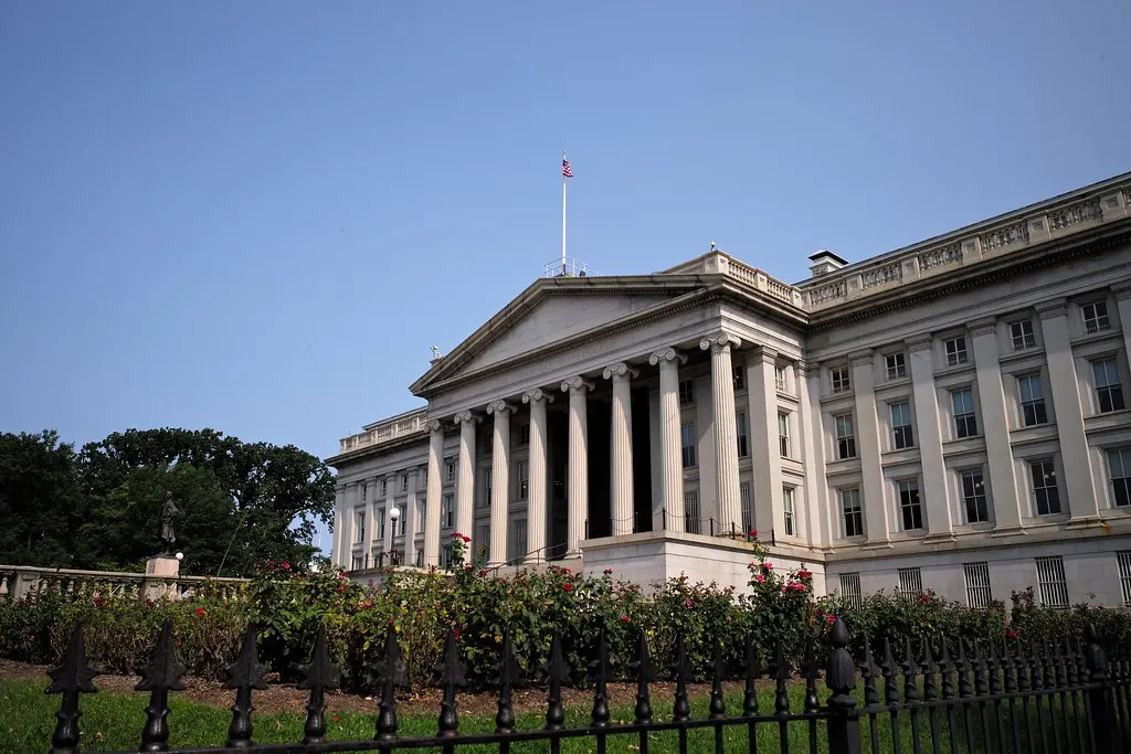 The facade of the United States Department of the Treasury building with neoclassical columns and a flag on top.